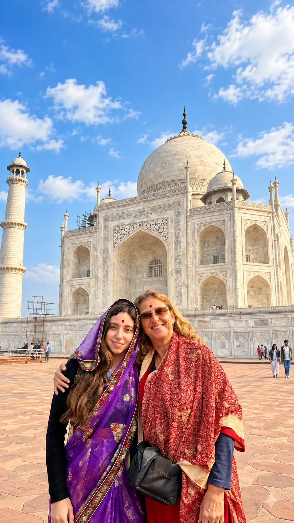 Two foreign female tourists wearing traditional Indian sarees posing in front of the Taj Mahal in Agra, India.