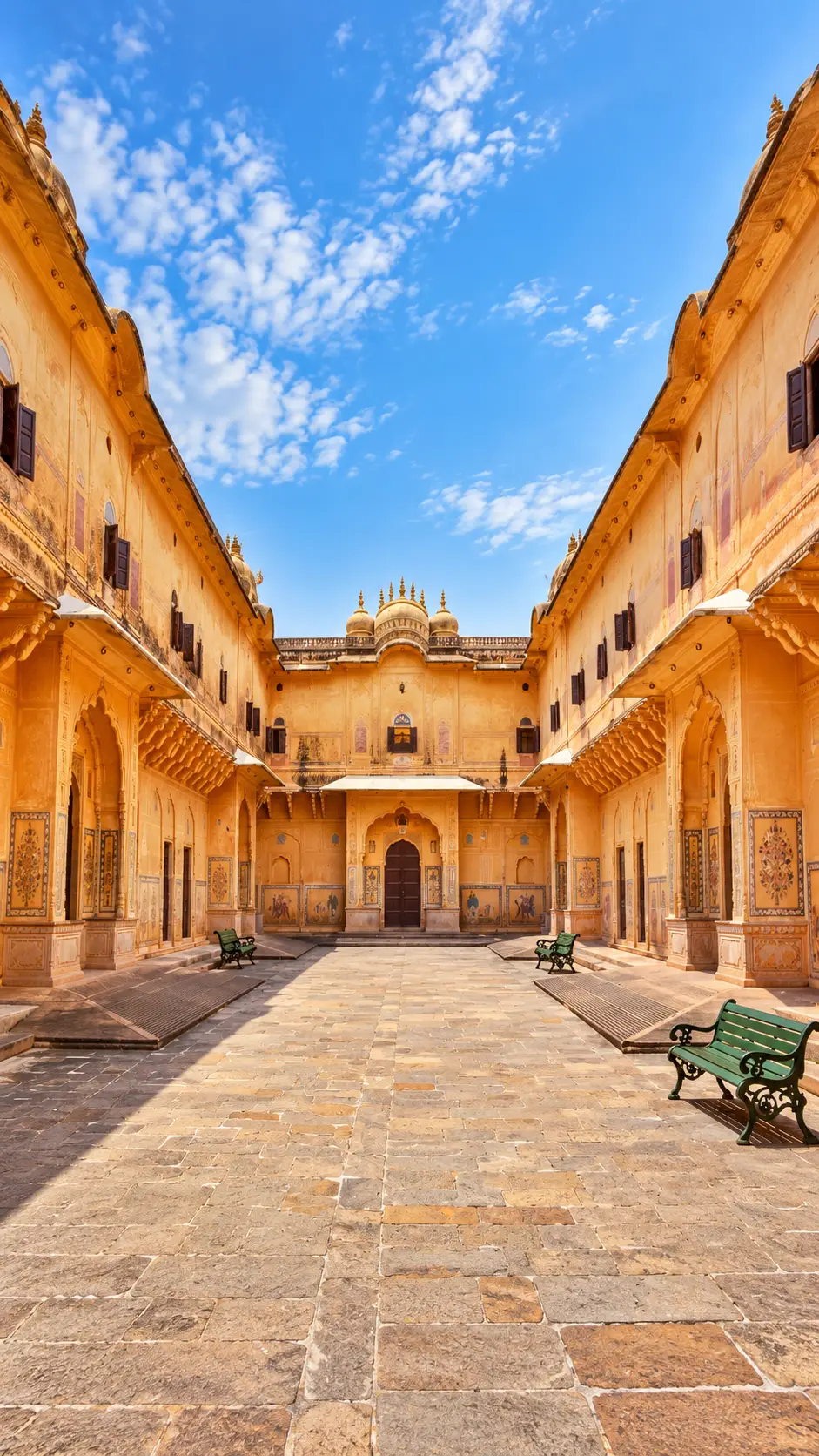 Ornate courtyard at Nahargarh Fort in Jaipur, Rajasthan, with golden walls, domes, and green benches.