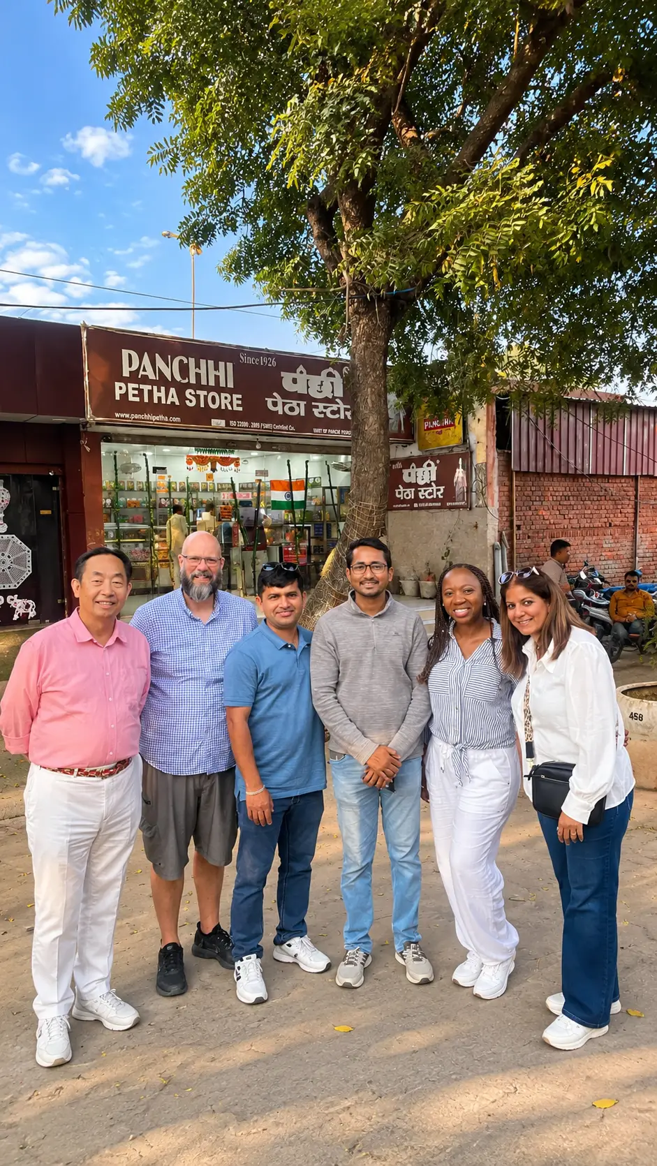 Five tourists posing with tour guide Riyaz Khan outside Panchhi Petha Store in Agra, India.