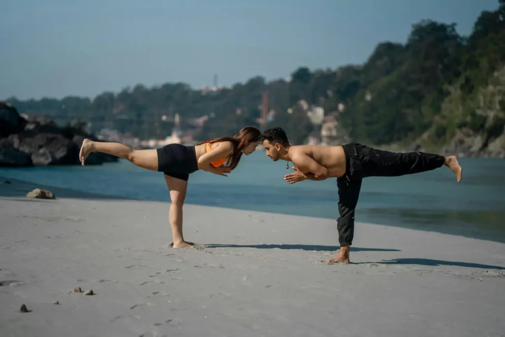 Couple doing yoga practice on bank of ganga river Ram Jhula Swarg Ashram Rishikesh Uttarakhand India