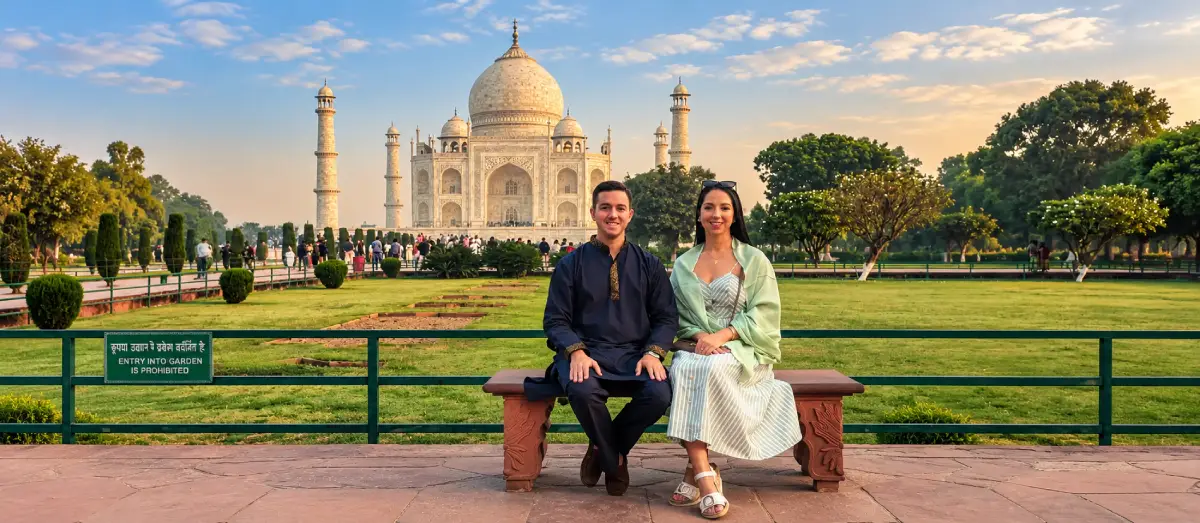 Tourist couple sitting on a bench with the Taj Mahal in the background in Agra, India.